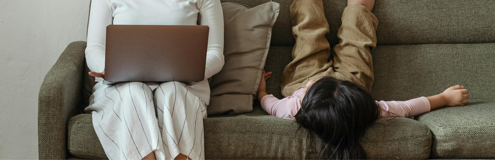 En mamma och barn sitter i en soffa, mamman har en dator i knät.