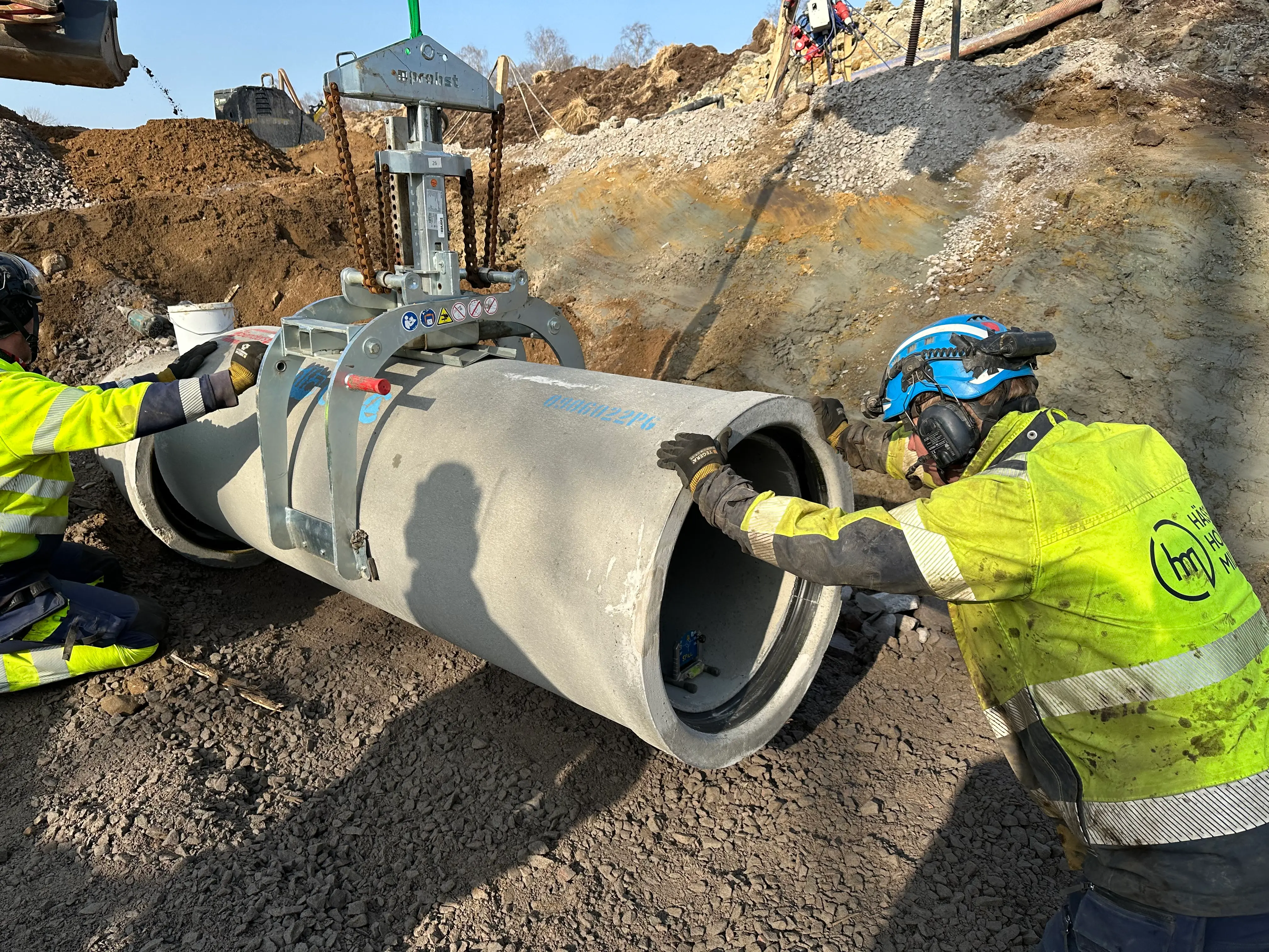 En person i varselkläder och blå hjälm som puttar på ett stort betongrör.